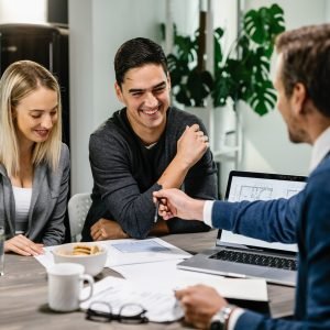Happy couple having a meeting with real estate agent and analyzing blueprints while communicating.
